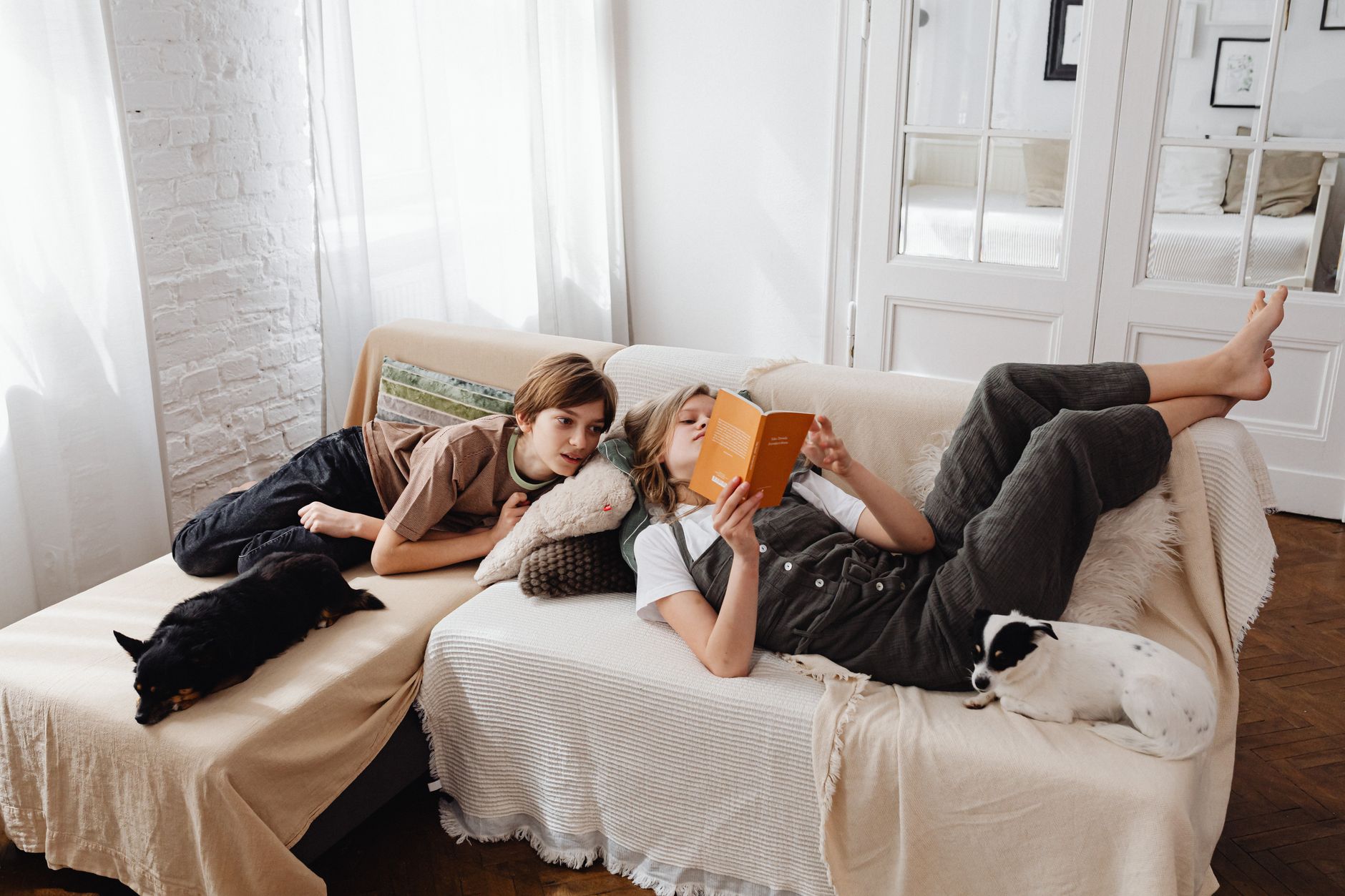 Kids relaxing on the sofa with dogs, enjoying a book in a warm, indoor setting.