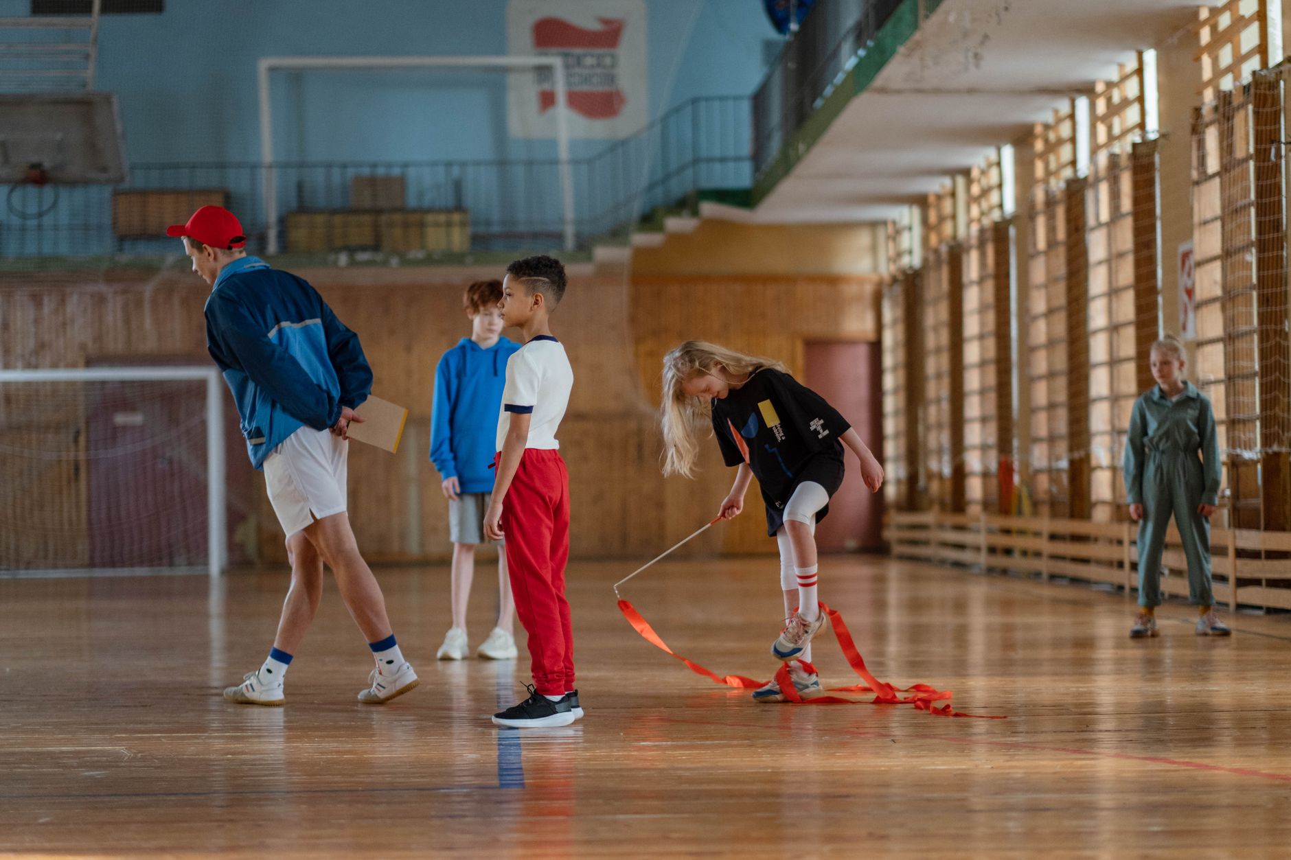 Children practicing gymnastics in a sports hall with their teacher.