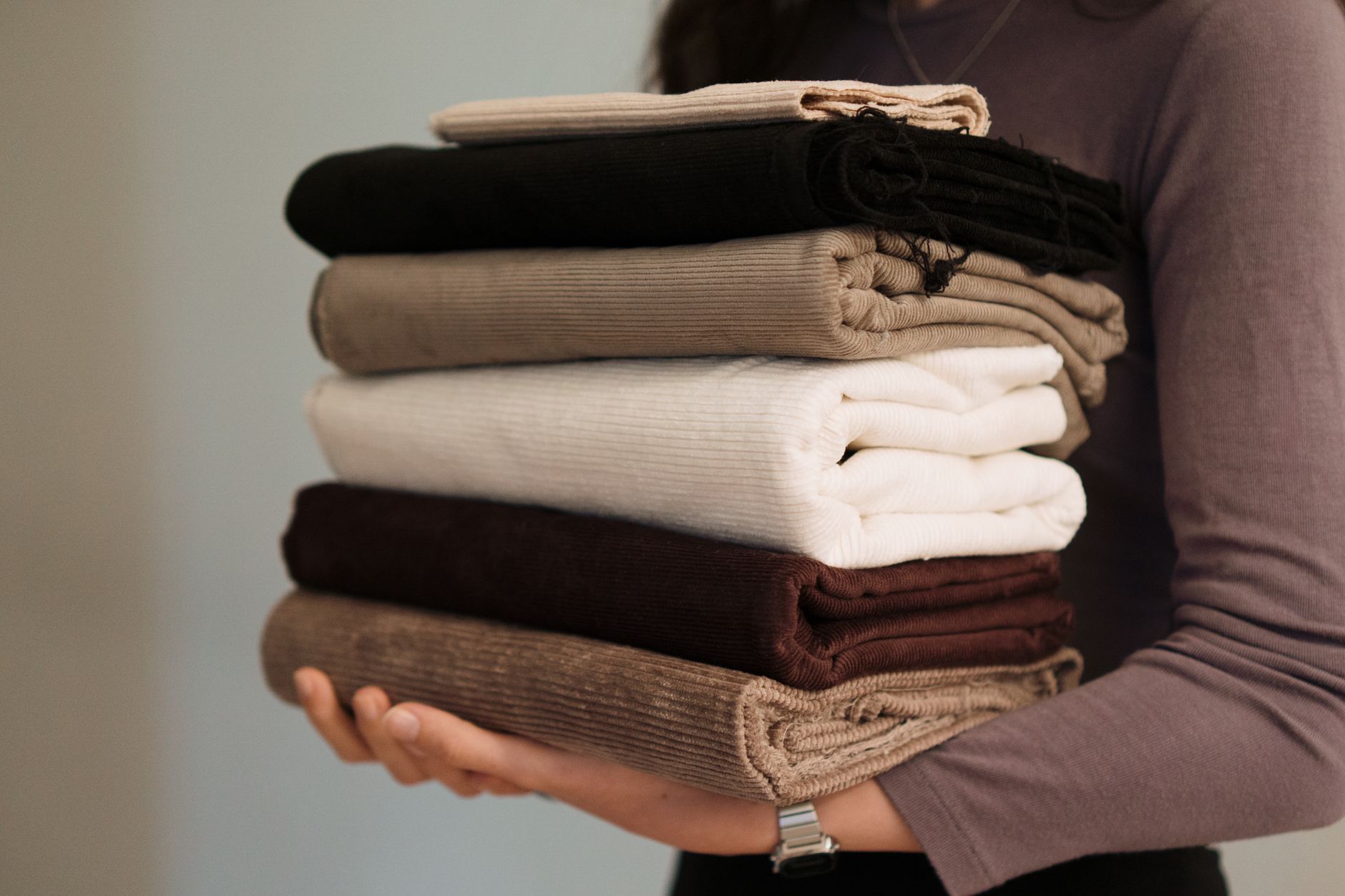 Close-up of hands holding a stack of folded neutral-toned fabrics, ideal for textile projects.