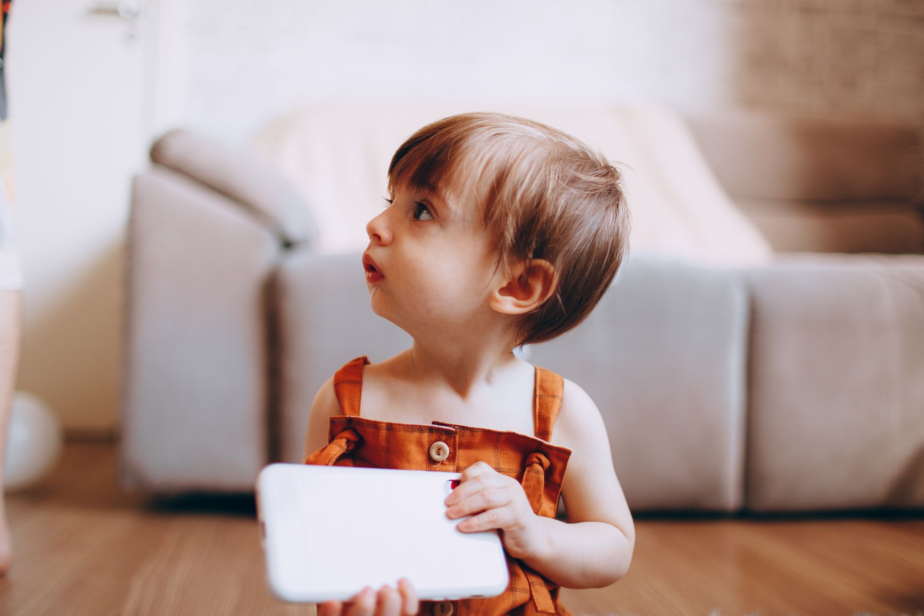 Adorable toddler holding a tablet indoors, looking curiously to the side.