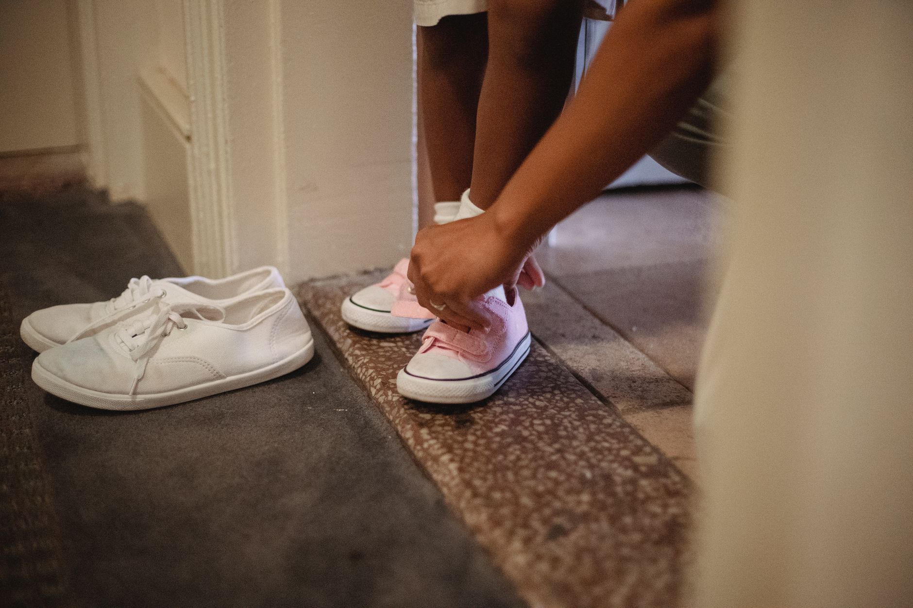 Unrecognizable ethnic mother helping anonymous kid to put on footwear while standing in corridor in apartment before going on street