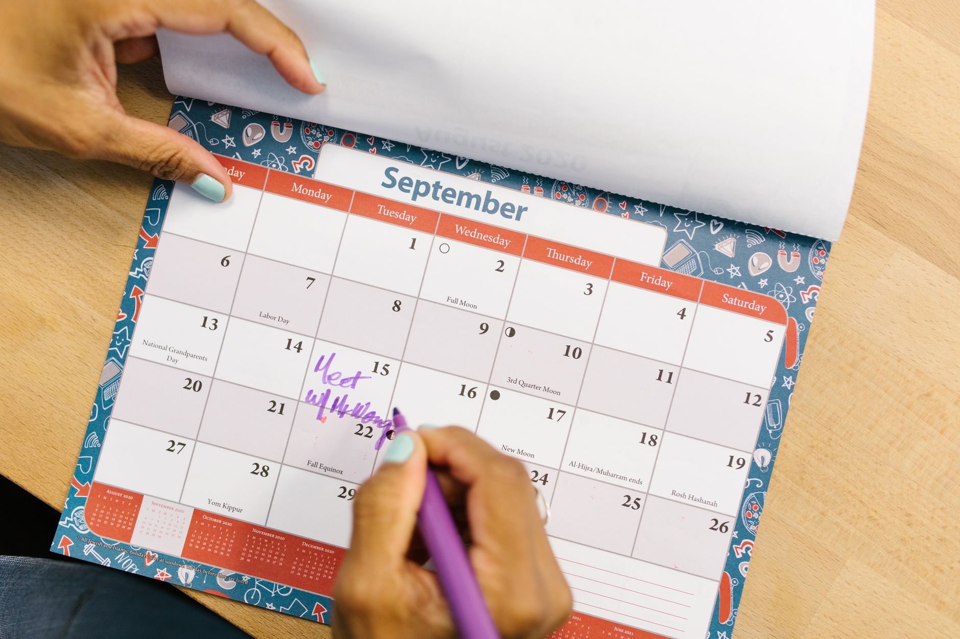 A person marking a calendar in September with a purple pen on a wooden desk.