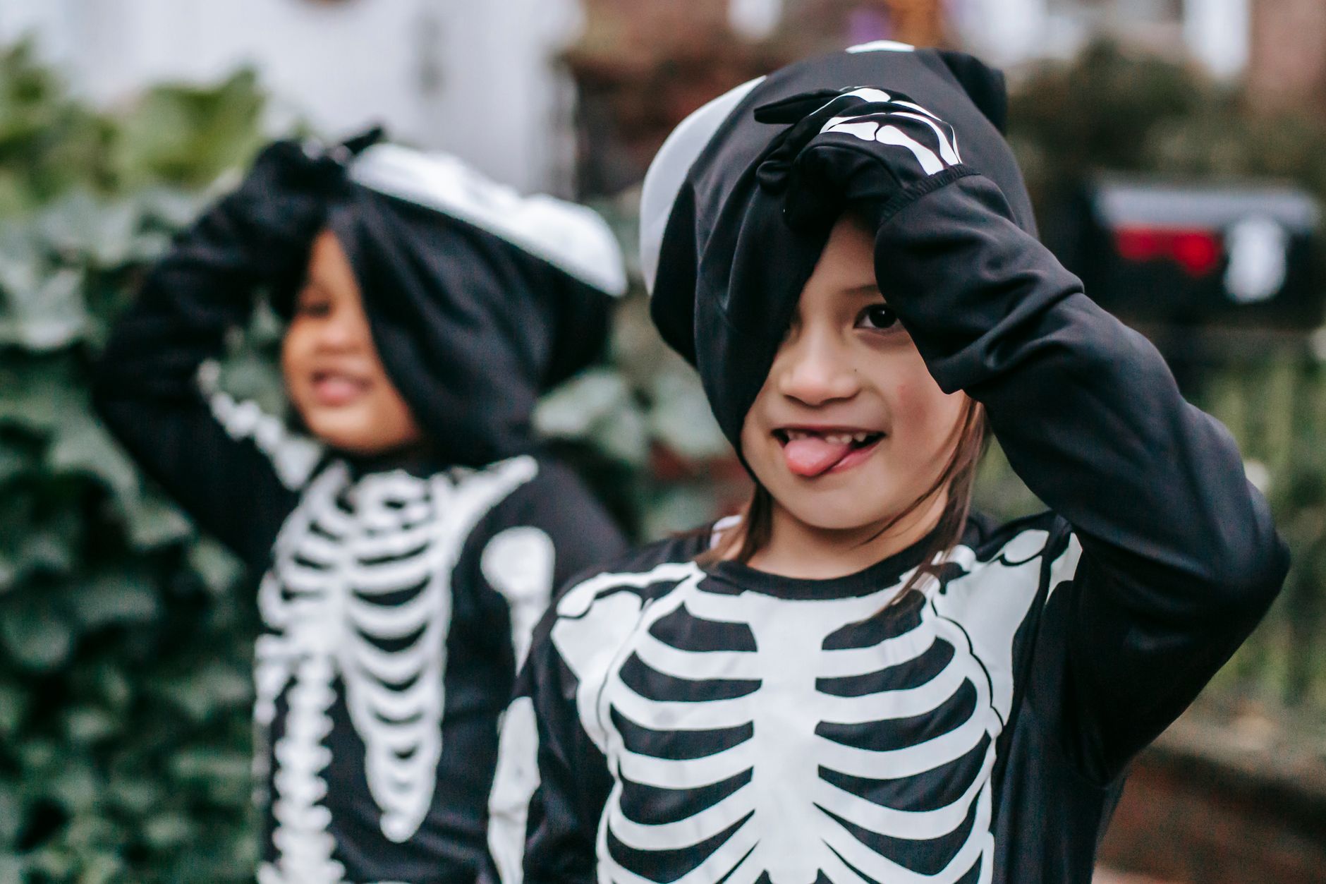 Multiethnic children in black skeleton costumes and masks making funny faces while standing in street in daytime