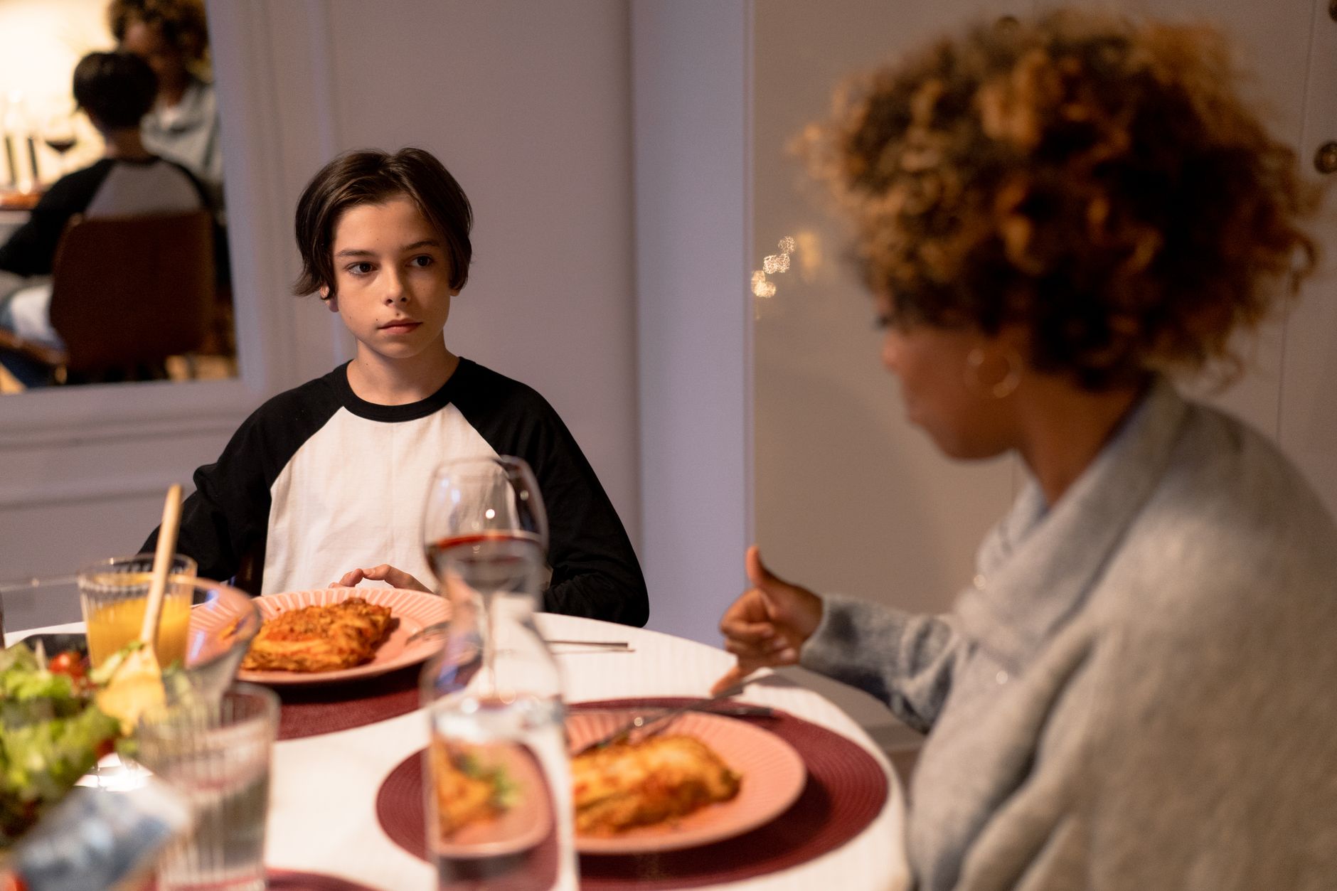 Family gathering around the dinner table enjoying pasta and drinks. Emotional connection and conversation.