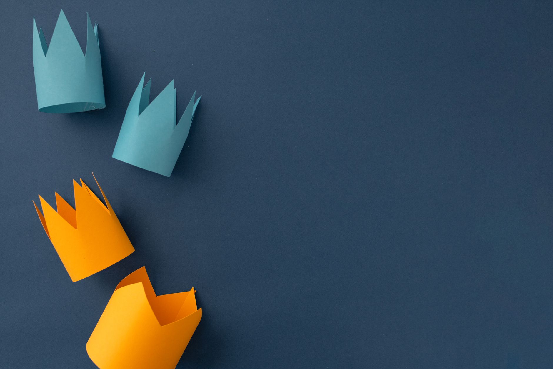 Vibrant paper crown cutouts arranged on a dark blue background with ample copy space.
