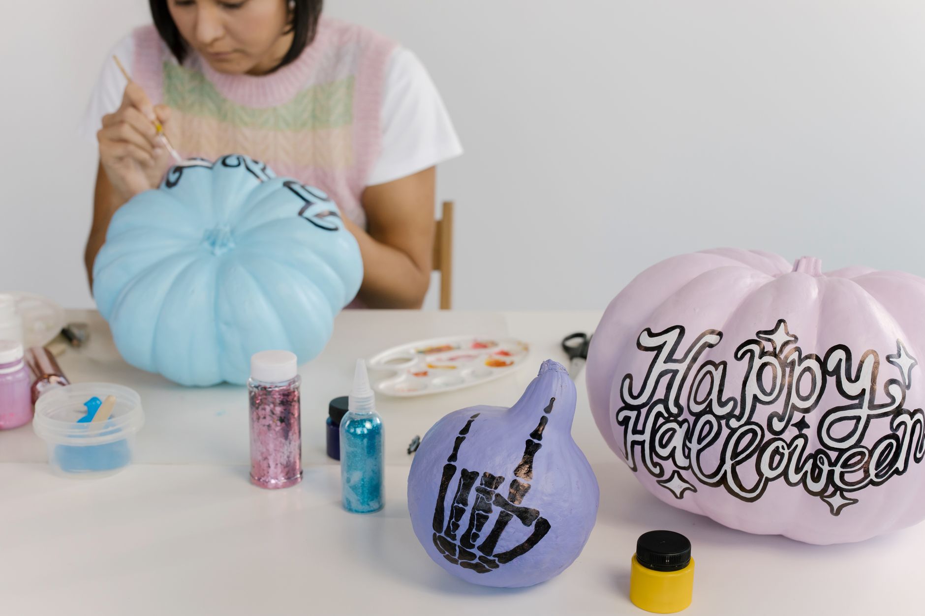A person painting pastel Halloween pumpkins with designs and text at a crafting table.