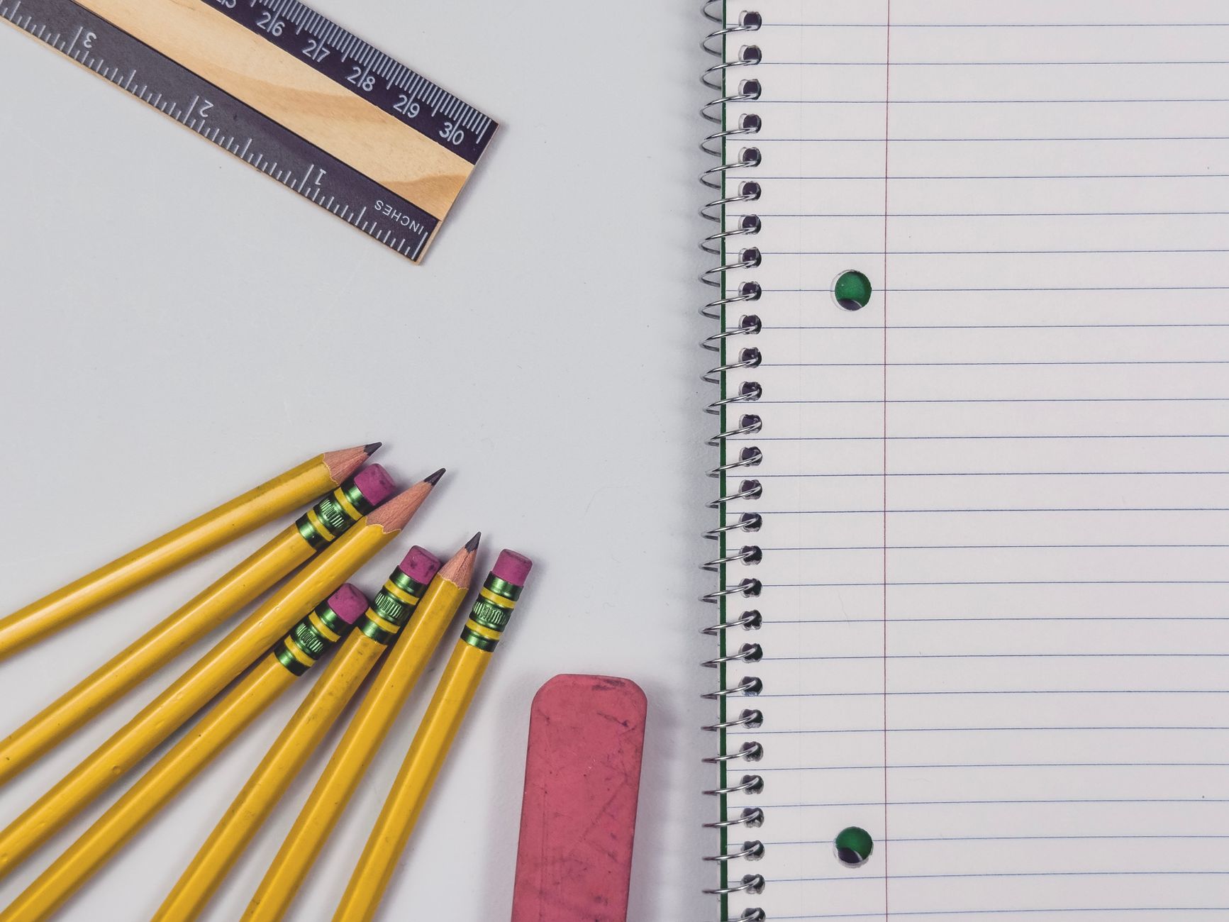 A neat arrangement of yellow pencils, eraser, ruler, and spiral notebook on a flat surface, perfect for educational themes.