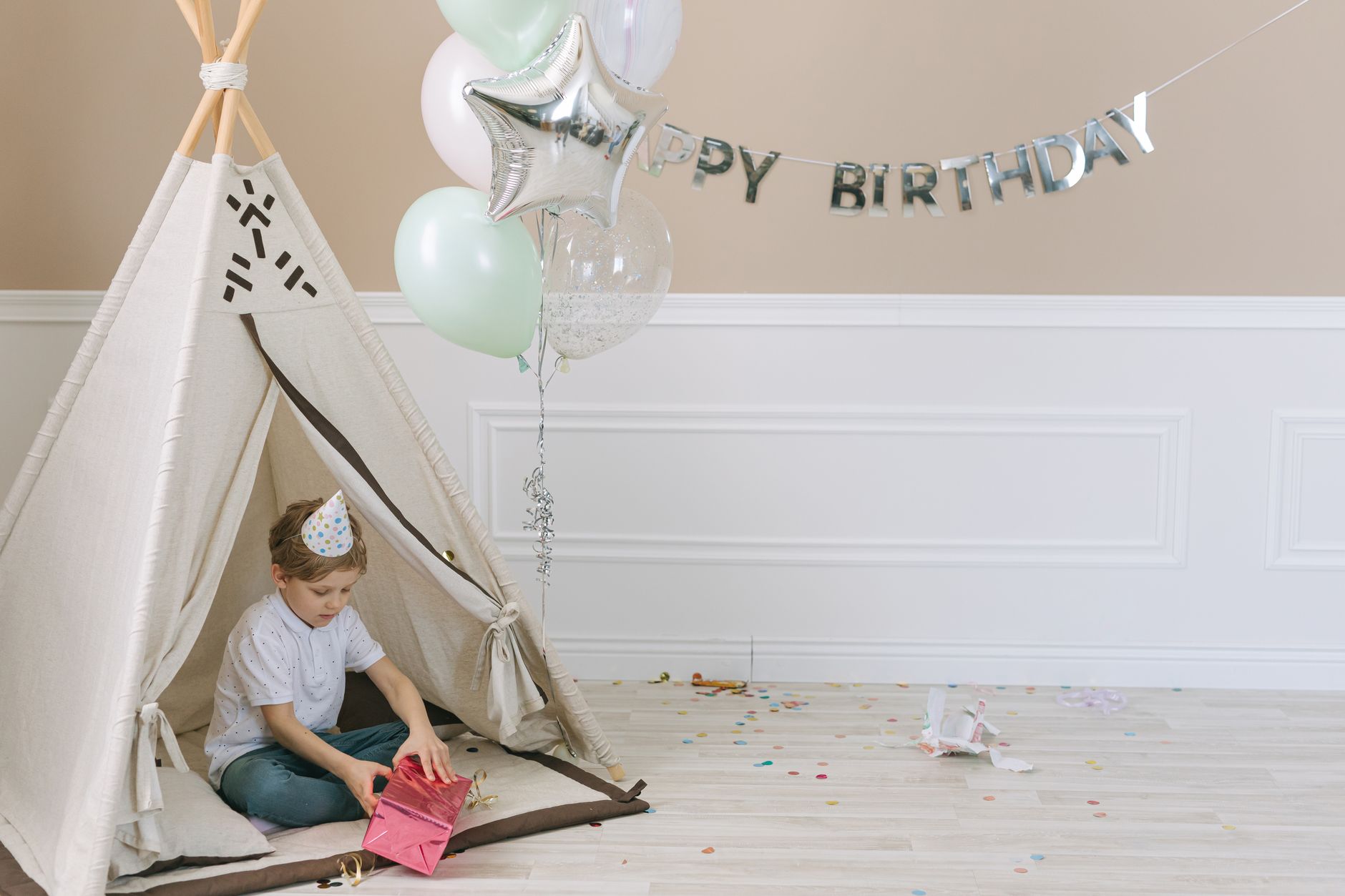 Child opening presents inside a teepee during a festive indoor birthday party.