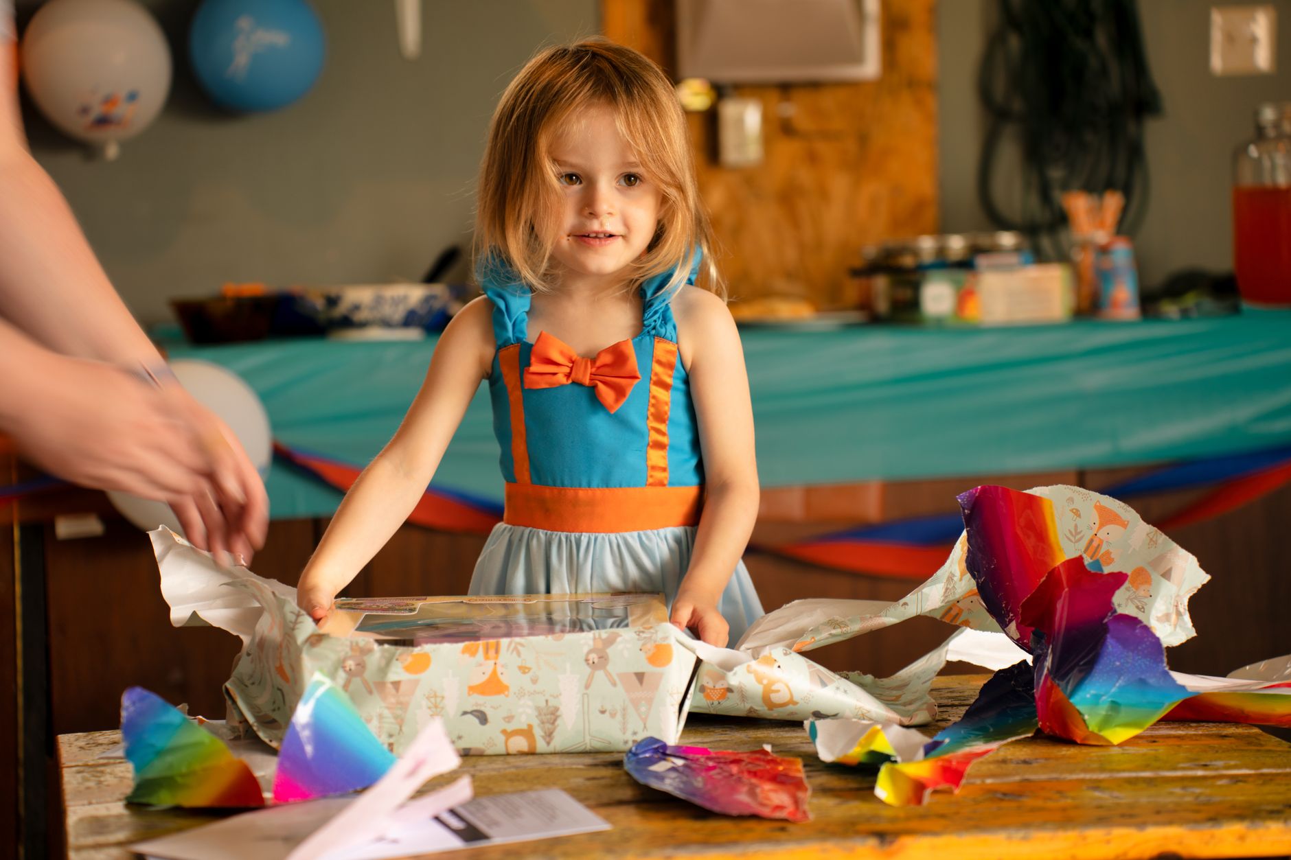A cheerful young girl excitedly opens birthday presents at an indoor party in Austin, MN.