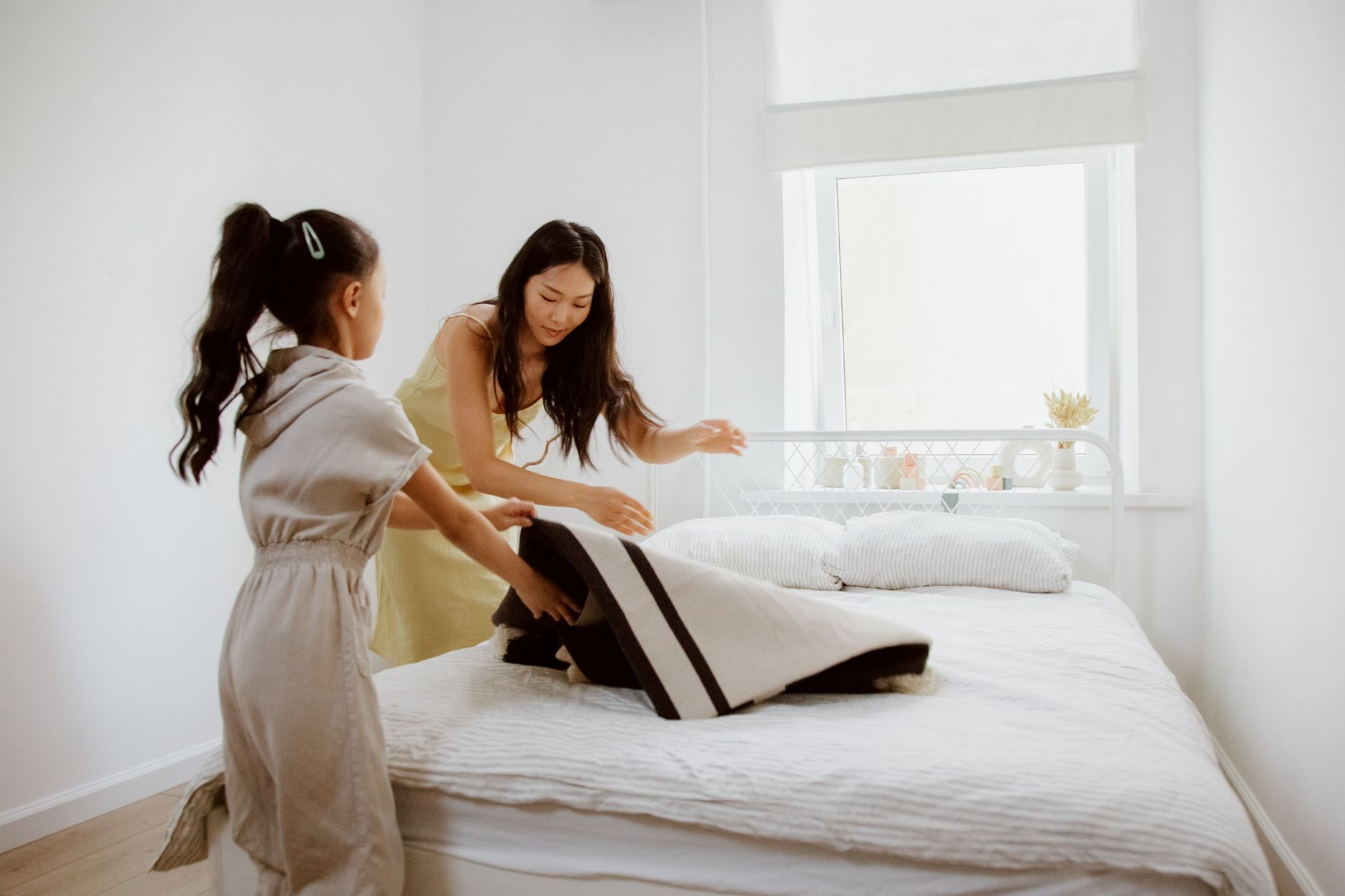 A mother and daughter collaborate to make a bed, promoting family bonding and home care.