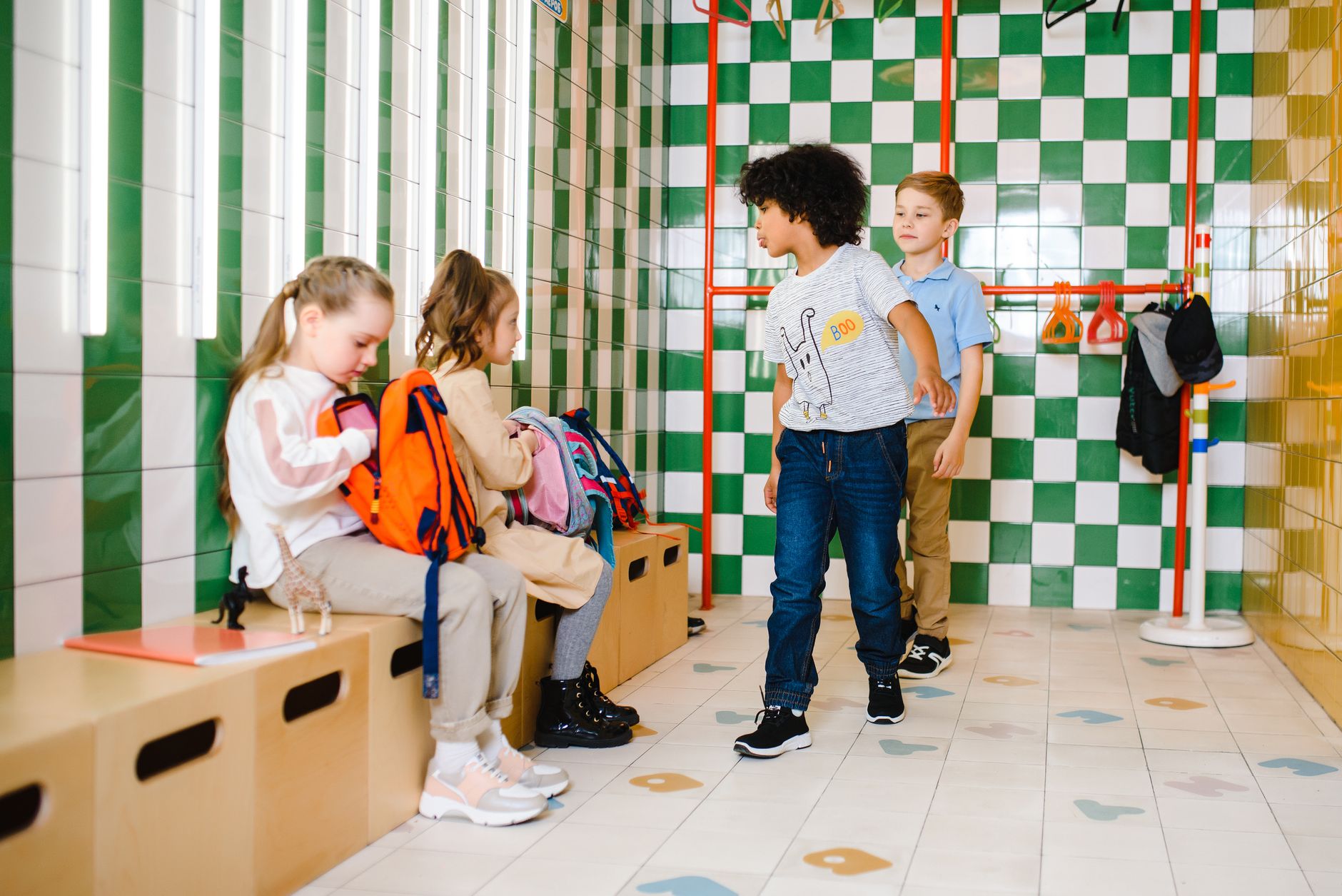 Group of children in a colorful school hall checking their backpacks.