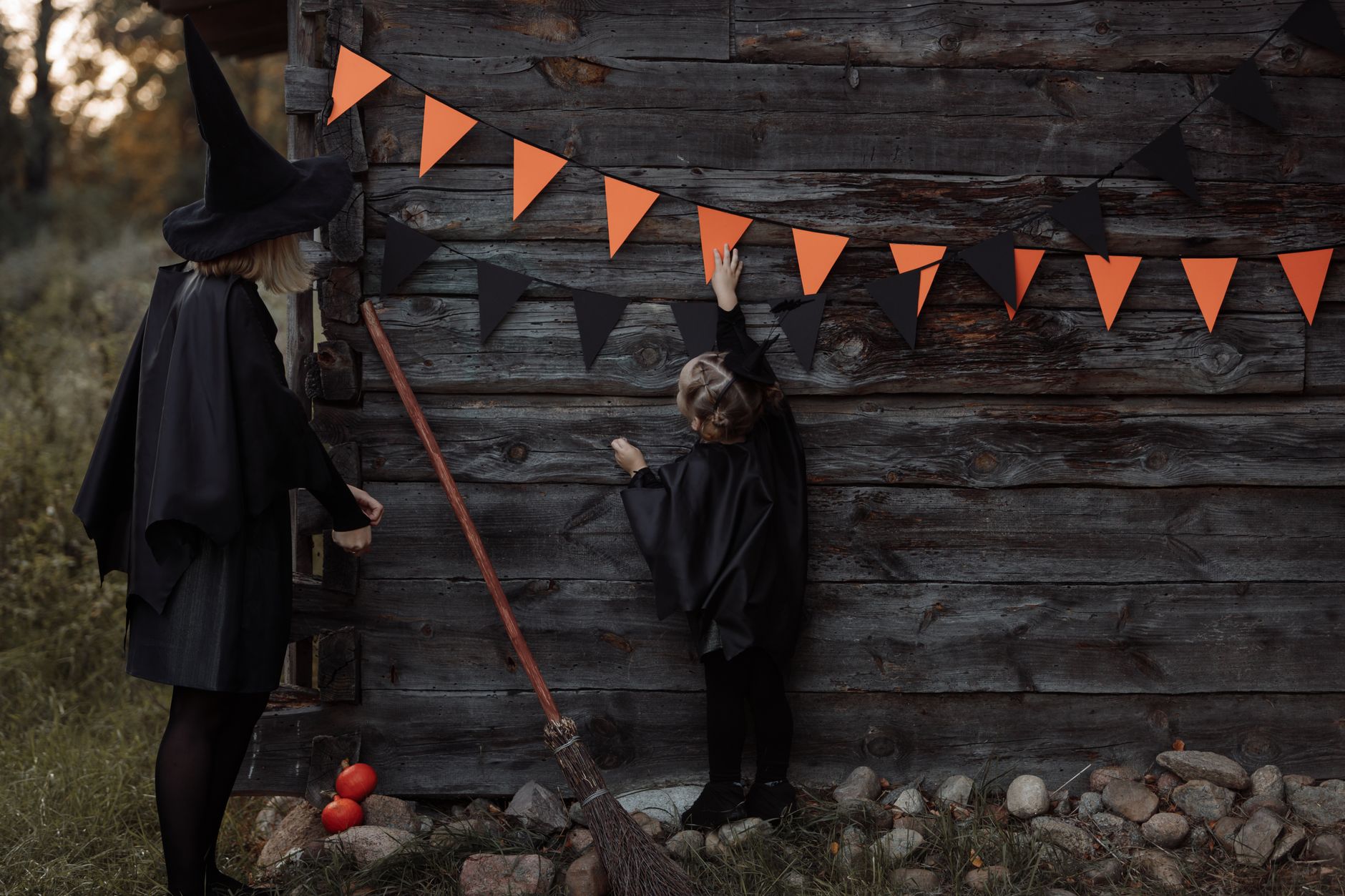 A mother and daughter in witch costumes hang pennant banners on a wooden wall for Halloween.