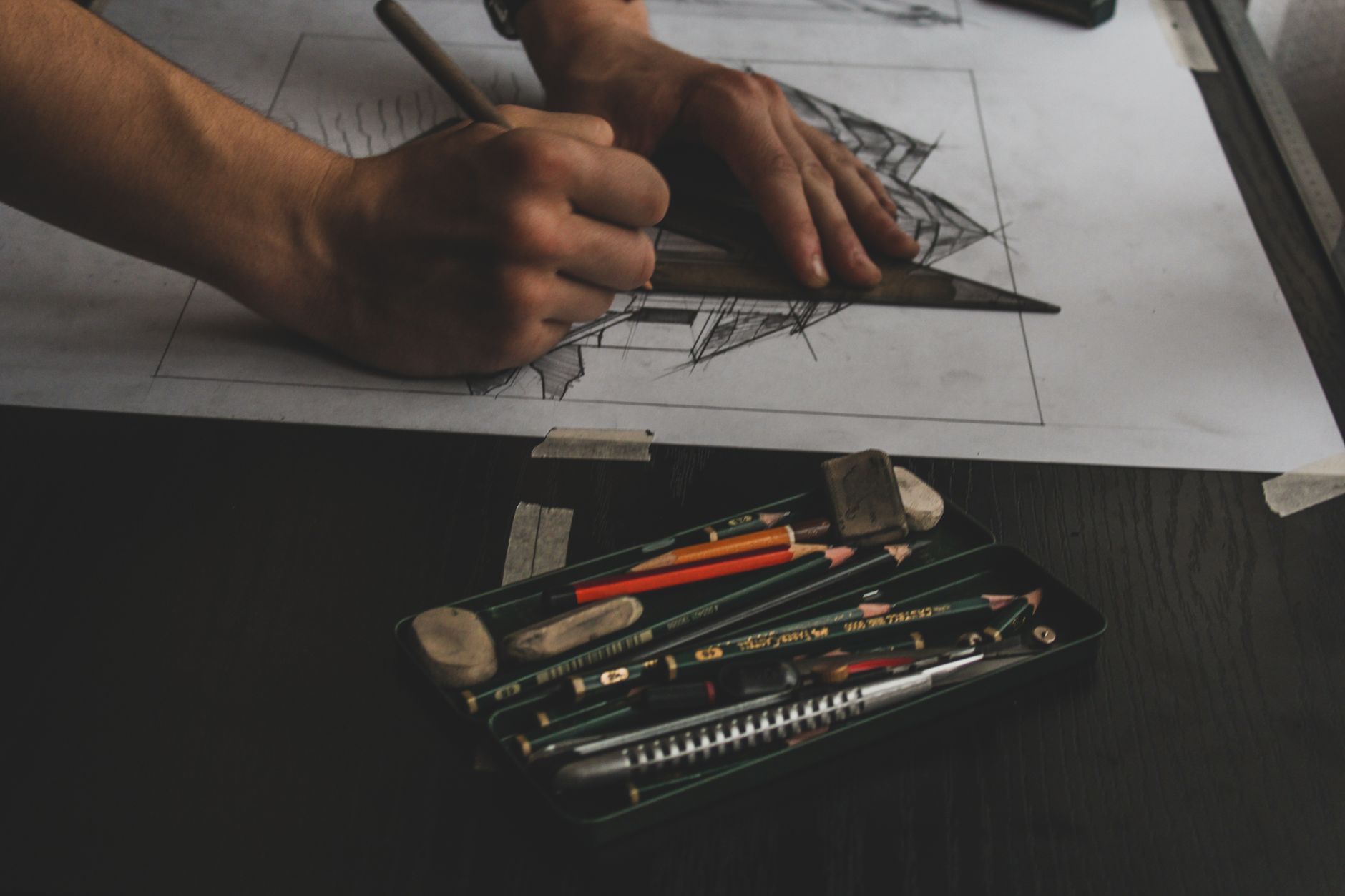 Hands working on a detailed sketch with pencils and erasers, showcasing artistic focus.