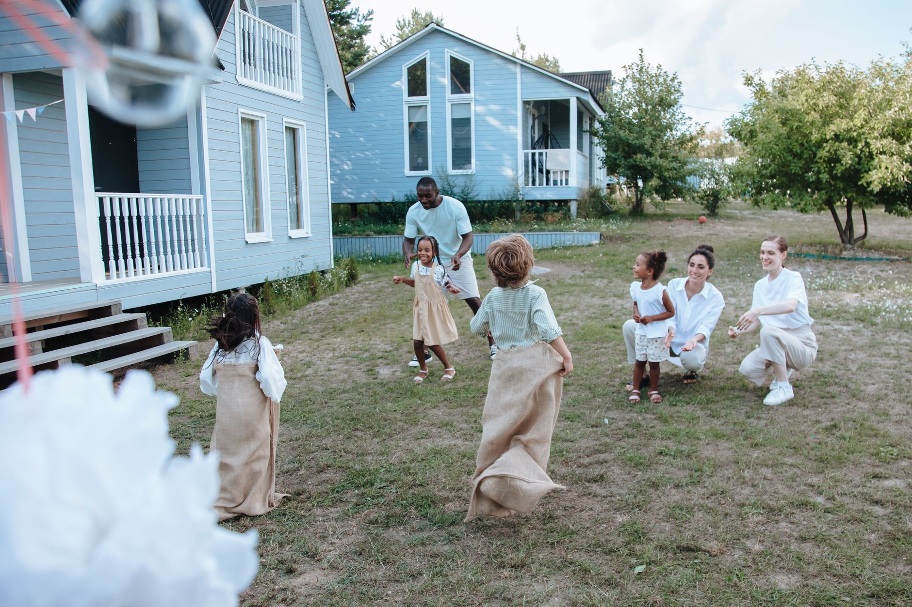 Children and adults have fun with a lively sack race outside a cozy home on a sunny day.