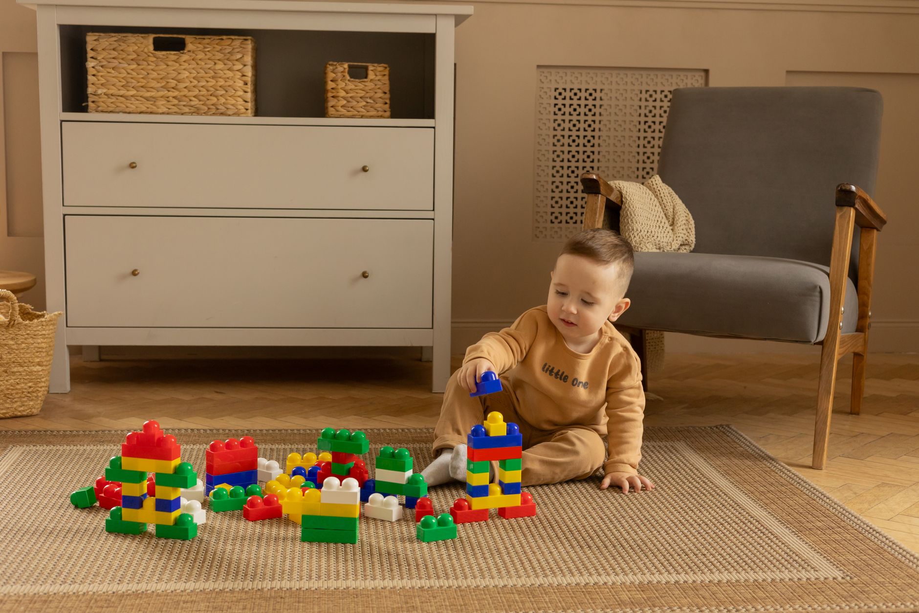 A young boy playing with colorful building blocks on a rug in a cozy room.