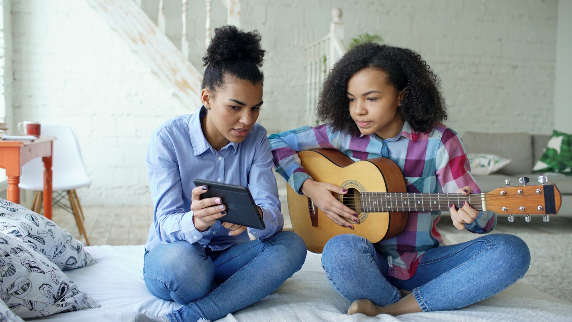 A mother and daughter sitting on a bed, enjoying guitar music together.